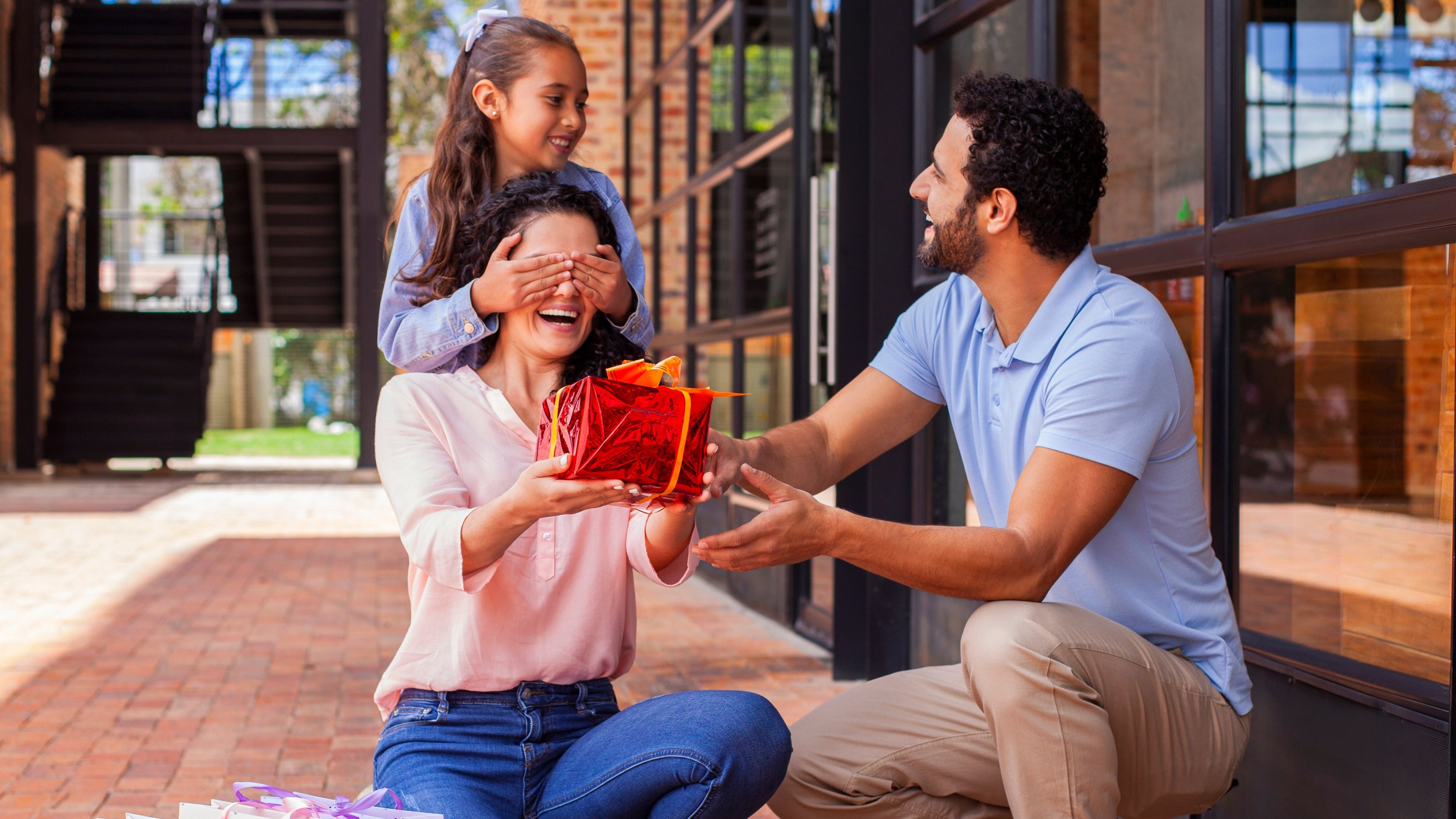 Padre, esposa e hija en una escena familiar dándole un regalo a la madre.